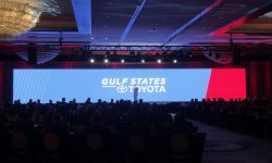 A speaker presents onstage at a Gulf States Toyota event in front of a large LED screen with a seated audience in a dimly lit ballroom.