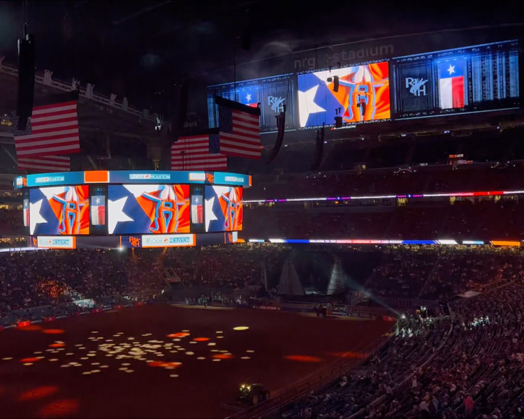 Stadium interior during an event with large American flags and digital screens showing RODEOHOUSTON graphics.