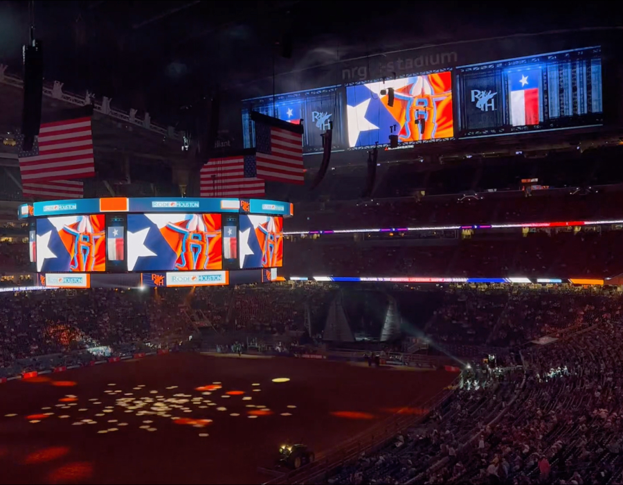 Stadium interior during an event with large American flags and digital screens showing RODEOHOUSTON graphics.