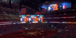 Stadium interior during an event with large American flags and digital screens showing RODEOHOUSTON graphics.
