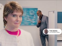 A woman in focus smirking playfully with a man in the background pointing and smiling, identified as "The Boss" in a caption.