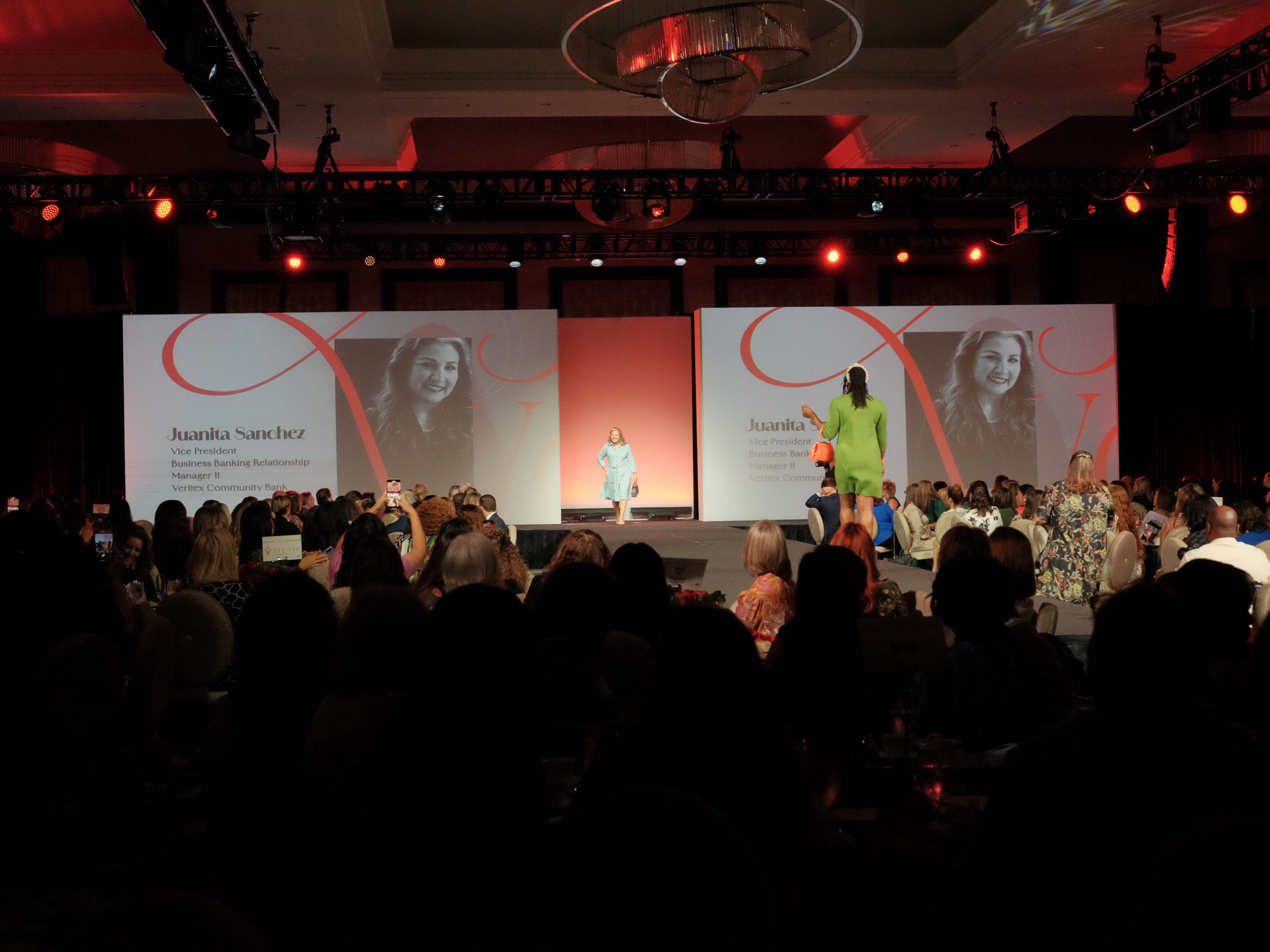 A vibrant runway show at Women in the Fast Lane of STEAM, featuring Juanita Sanchez's profile on screens, with attendees engaged in the event.