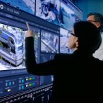 Two security professionals analyze surveillance footage on a large screen displaying i-PRO’s Active Guard system, which monitors multiple feeds and data.